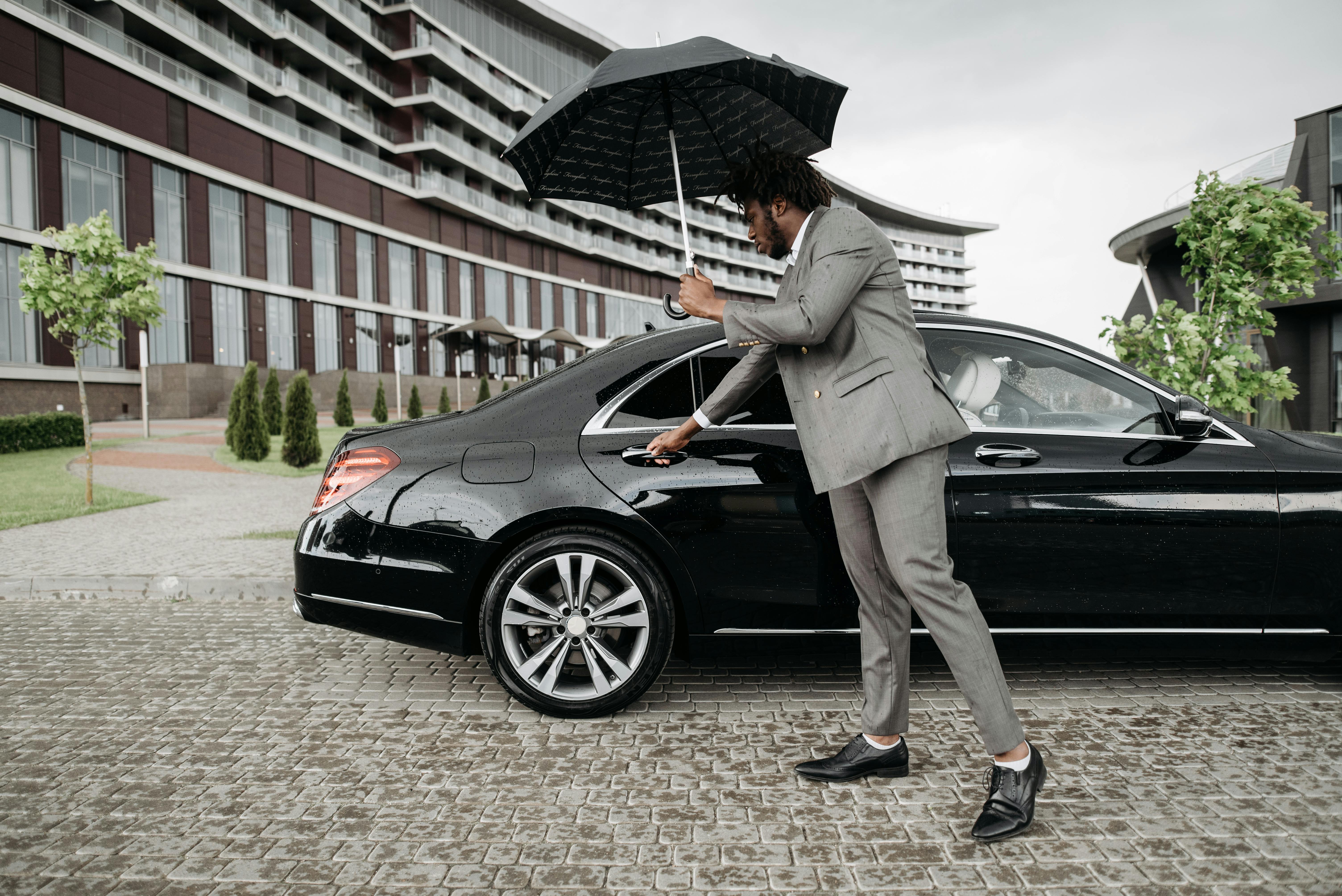 Professional chauffeur opening car door with umbrella
